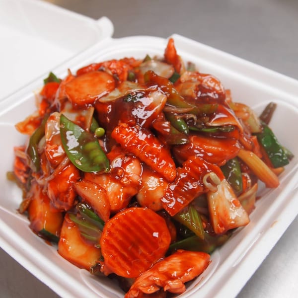 Sweet and sour chicken with vegetables in a white takeout container from Three Happiness Express.